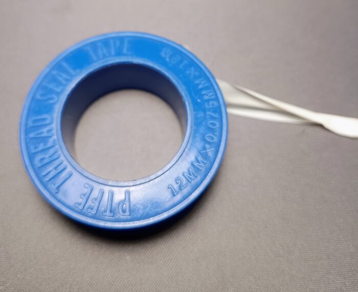 Blå rulle med teflongängtape, använd för tätning av gängor vid bygg- och renoveringsprojekt, mot en grå bakgrund.