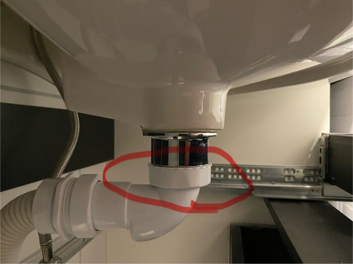 Kromad del under handfat med röd markering; potentiellt läckande vattenlås som kan kräva byte av packning eller utloppsvinkel.