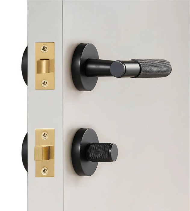 Svart dörrhandtag och vred i minimalistisk stil på en grå dörr med guldfärgade låsdelar.