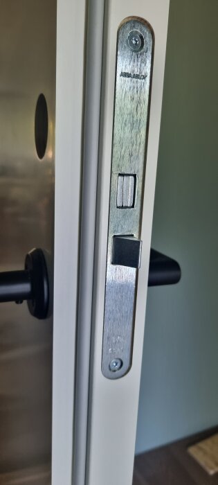 Närbild av dörr och låshus, märkt Assa Abloy, med ett svart dörrhandtag synligt.
