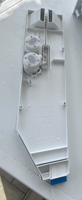 Bild på en Bosch i-DOS tvättmedelsbehållare, vit med blå detaljer, liggande på ett bord.