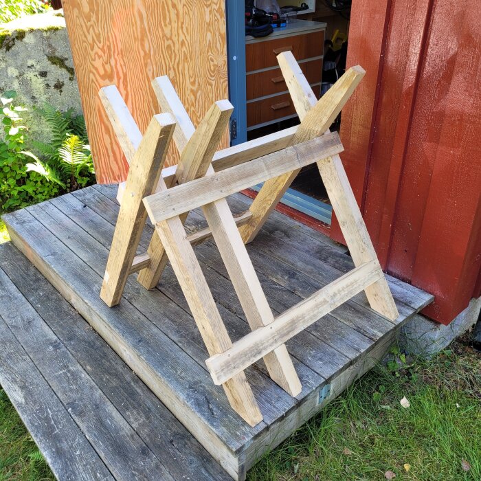 Hopfällbar sågbock av spillvirke på en träveranda framför en öppen dörr, bredvid rödmålad vägg.