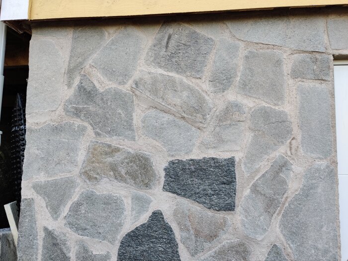 Grå stenvägg av miniskiffer på attefallsstuga, fogad med putsbruk.