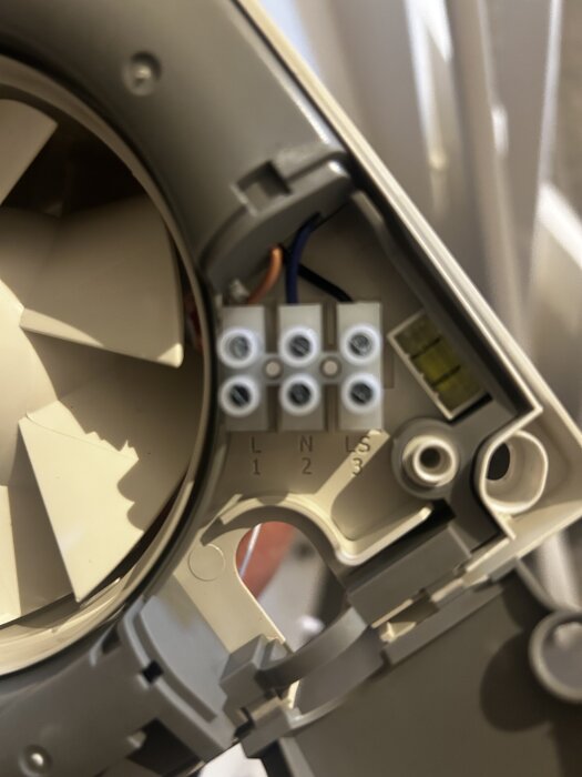 Badrumsfläkt med närbild på kopplingsplint märkt L, N, S för kabelanslutning, med synliga blå och bruna kablar.