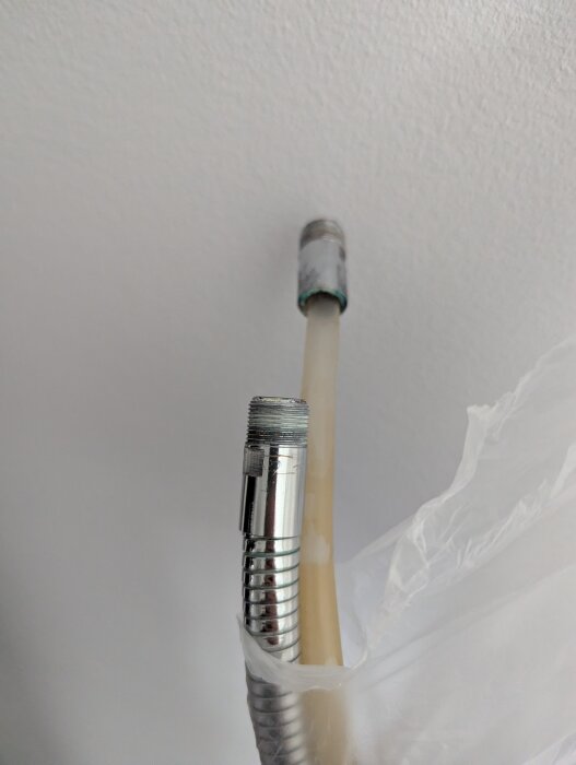 Flexibel metallslang och plastslang med metallanslutningar, fotograferad från sidan. Kan vara en duschslang från ett inbyggt badkar.