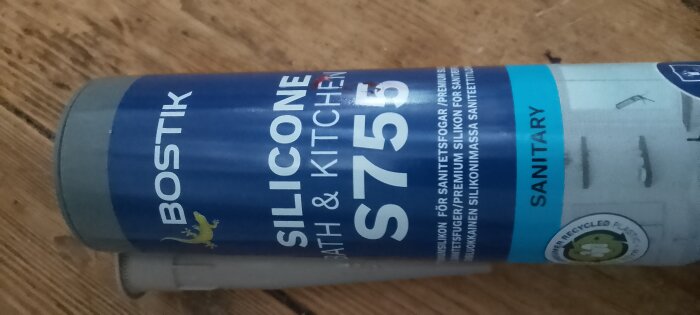 Bostik silikonpatron med etikett "Silicone Bath & Kitchen S755", fotograferad på trägolv. Färg diskrepans nämns i beskrivningen.