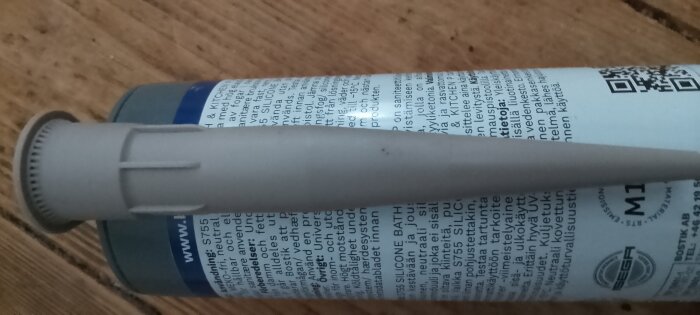 Grå silikonförpackning från Bostik med text och sprutspets på en trägolvbakgrund.