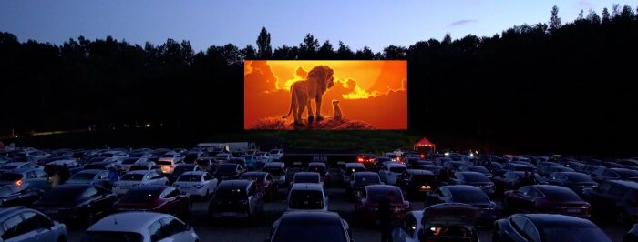 Bilar parkerade framför en stor bioduk utomhus i en drive-in-bio på kvällen.