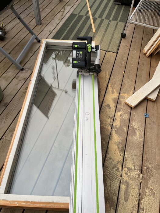 Fönsterkarm med sänksåg på trädäck, omgiven av träspån och byggmaterial.