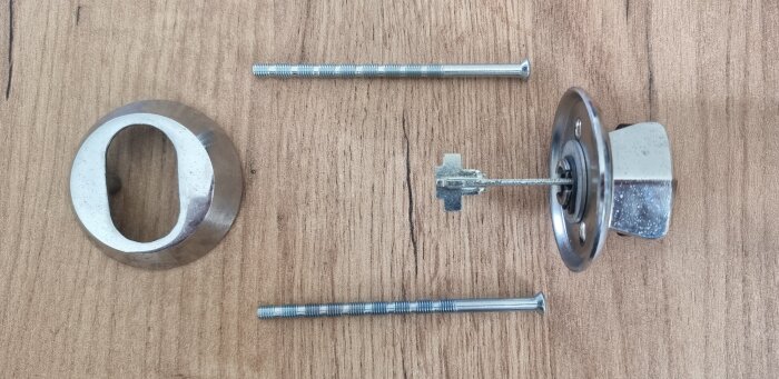 Cylinderlås och delar på träbord, inklusive skruvar och cylinderring, för diskret installation och säkerhet vid behov av upplåsning utifrån.