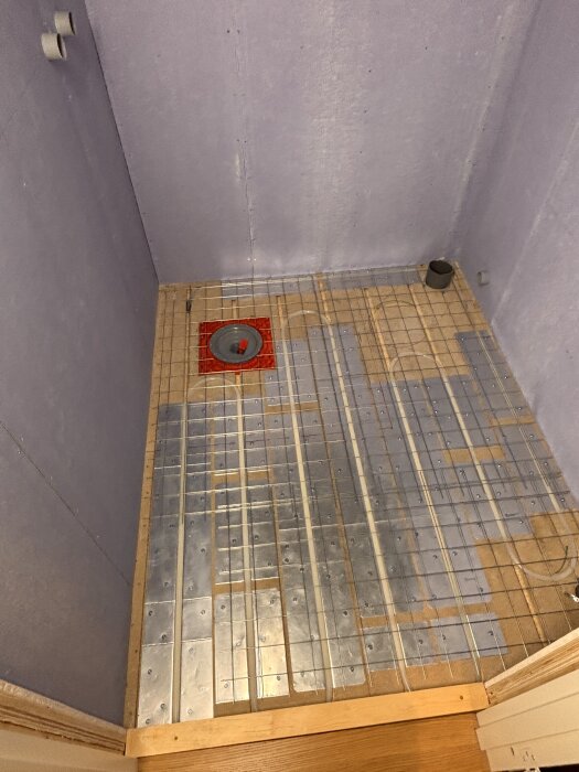 En dusch med lutande undergolv, byggt av plattor och armeringsnät över trä. En golvbrunn är installerad, redo för vidare renovering.