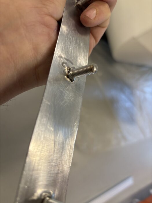 Närbild på en hand som håller en metallremsa med bultar, använd för att montera baklyktor och handtag på en vagn.