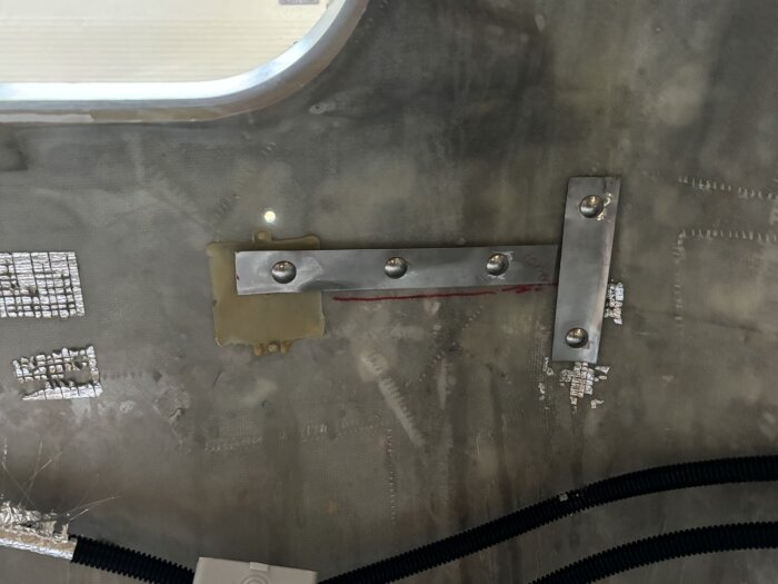 Metallplåtar monterade på insidan av en yta, med bultar och elslangar synliga runt omkring.