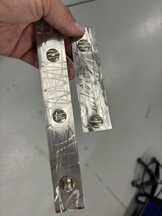 Rostfria plåtremsor med fyrkantiga bultinflikningar, anpassade för montering av handtag och baklyktor, hålls i hand.