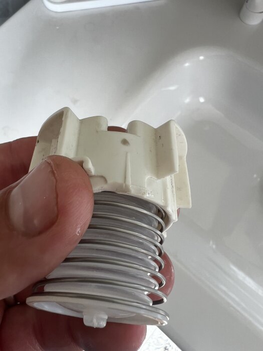 Hand håller en krackelerad plastdel på en knapp till en toalett, synlig vid spolning.