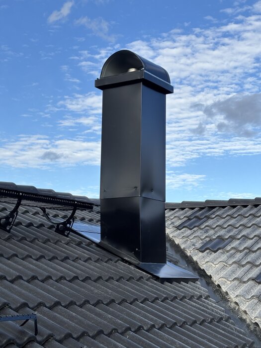 Sned skorsten på tegeltak under blå himmel.
