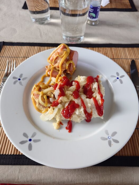 Tallrik med korv toppad med senap och en potatisgratäng dekorerad med ketchup.