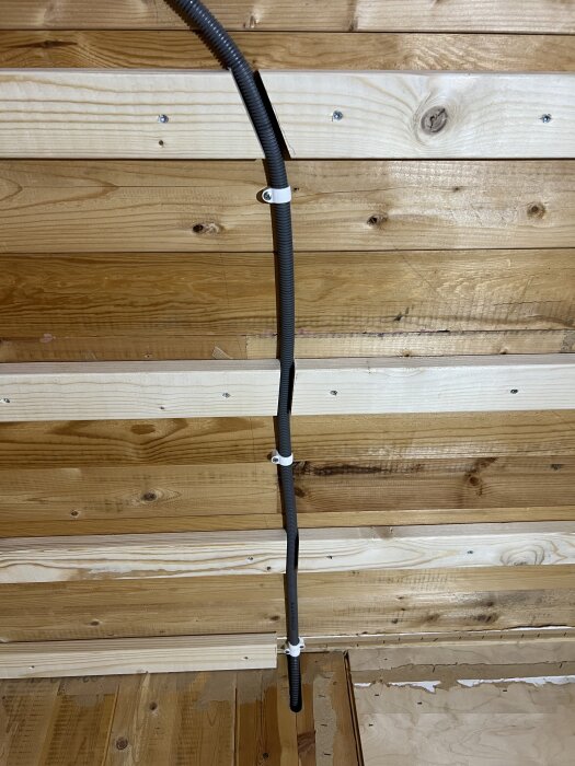 Elektrisk kabel dragen horisontellt längs en trävägg, fastsatt med vita kabelklämmor.
