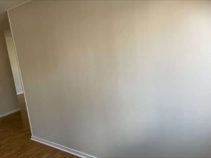 Vägg med vertikala linjer och misstänkt tapetkant vid listen, synliga luftbubblor. Trägolv och del av dörrkarm till vänster i bild.