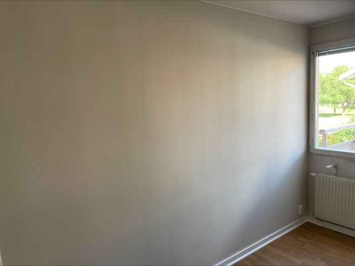 Vägg med synliga vertikala linjer och luftbubblor nära fönster med utsikt över trädgård. Målning verkar undermålig enligt inlägget.