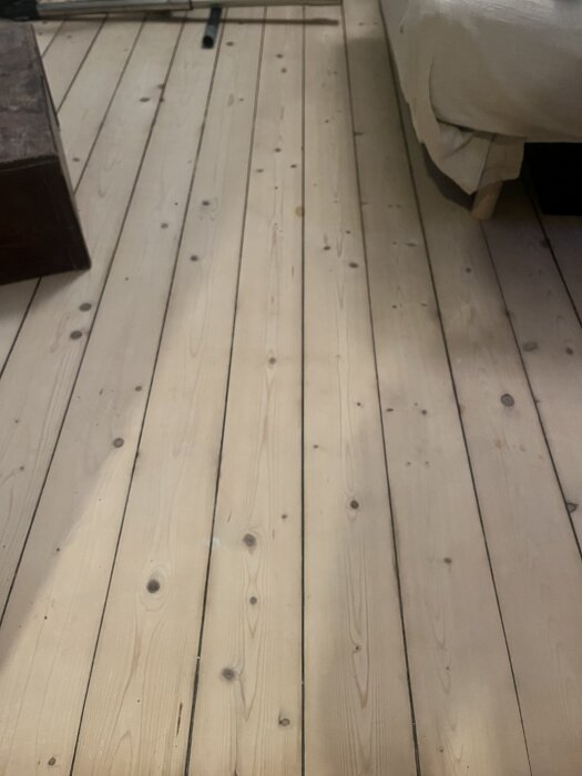 Ljust trägolv med synliga kvistar och plankor i ett rum med soffa och möbler.