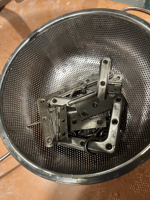 Metallbeslag i en trådsil efter att ha tumlats, redo för vidare behandling mot rost med citronsyra.