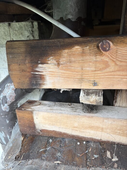 Träbjälkar med vattenfläckar, rostiga skruvar och ett metallrör under taket på farstukvisten. Synliga fuktproblem i konstruktionen.