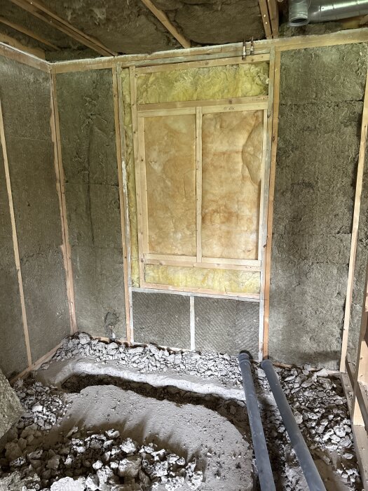 Renoverat 70-tals hus, visar väggisolering av trä och mineralull samt exponerade avloppsrör och rivet golv i ett rum.