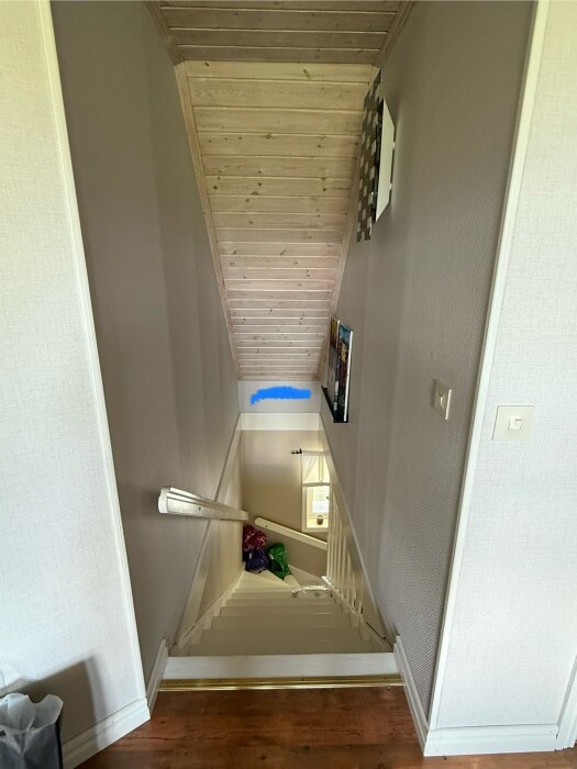 Trappa med vitmålat räcke och en blå markering på väggen där en luft-luftvärmepump planeras att placeras för värme och kyla till övervåningen.