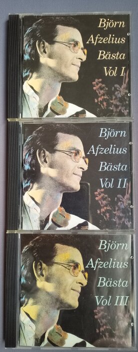 Tre CD-omslag för "Björn Afzelius Bästa", volymer I-III, med porträttbild av en man i profil och blomdetalj i bakgrunden.