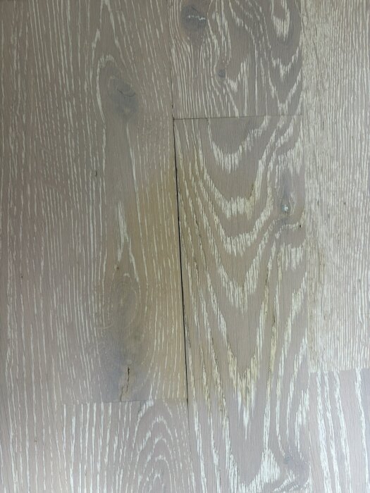 Vit ekparkett med gulaktiga vattenfläckar och små springor mellan plankorna.