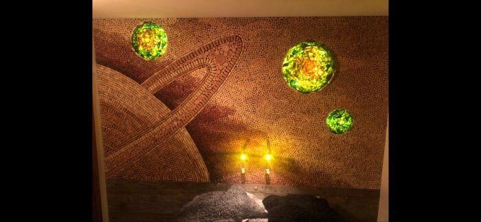 Dekorativ vägg i bastu gjord av vinkorkar med inlägg av gröna, lysande sfärer som liknar planeter eller stjärnor i ett konstnärligt mönster.