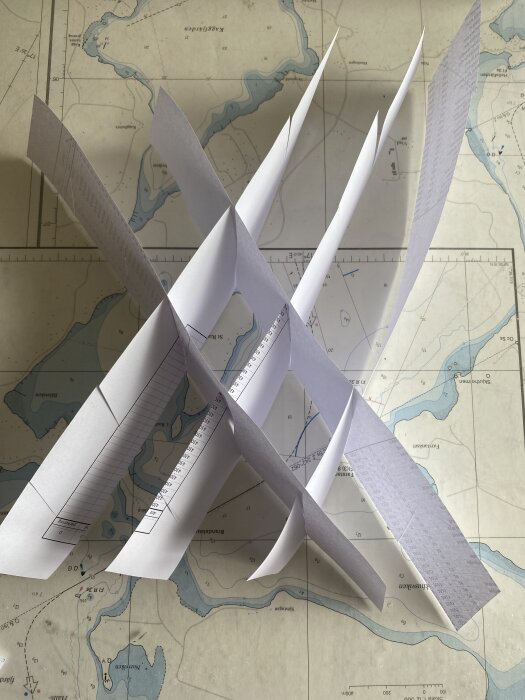 Pappersmodeller staplade i ett korsmönster på en karta över ett vattendrag, kanske en prototyp för ventilationsgaller.