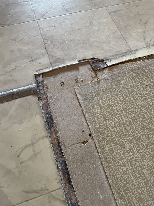 Gammalt vinylgolv med synliga skarvar och golvunderlag där en vägg har tagits bort.