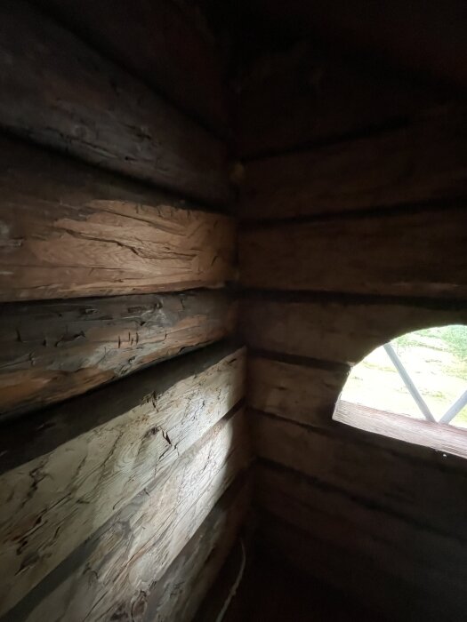 Väggar i en timrad struktur med träplankor, delvis belysta av ljus genom ett litet fönster i en träbyggnad.