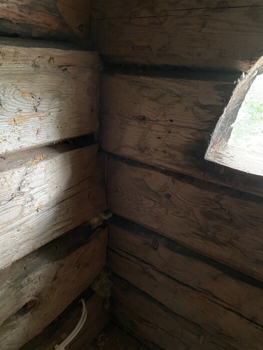 Vägg av gamla träplankor med sprickor och försämrad belysning, del av en renoveringssituation.