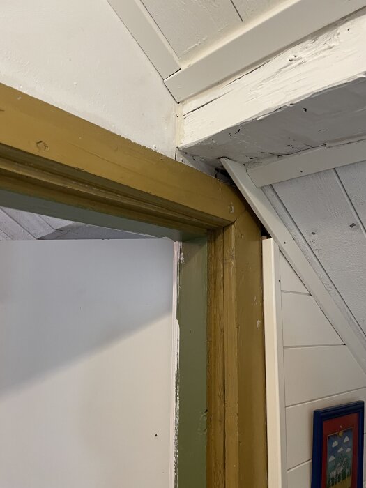 Dörrkarm och vägg i vitt och gult visar byggdetaljer, med en tavla delvis synlig i hörnet.