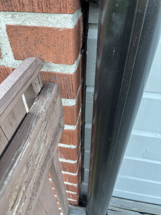 Glipa mellan träfasad och tegel med stuprör bredvid, risk för vatteninträngning.