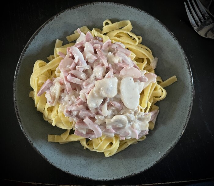 En tallrik med pasta tagliatelle och en krämig sås innehållande skinka, champinjoner och rädisor.