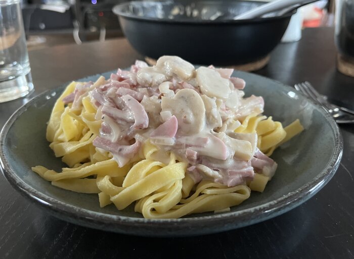 Tagliatelle med pastasås innehållande skinka, champinjoner, rädisor och lök serverad på en tallrik.