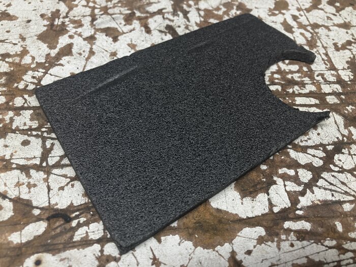 Svart 6 mm depron-skiva med utskuren del, liggande på färgstänkt yta.