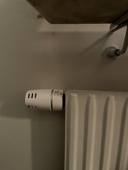 Otroligt nog saknas färg runt ett vitt radiatorrör med termostat i ett vardagsrum.