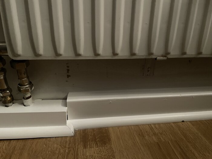 Ovanför en vit golvlist syns ett element där väggen bakom inte blivit målad ordentligt, vilket avslöjas av synliga fläckar kring elementet.