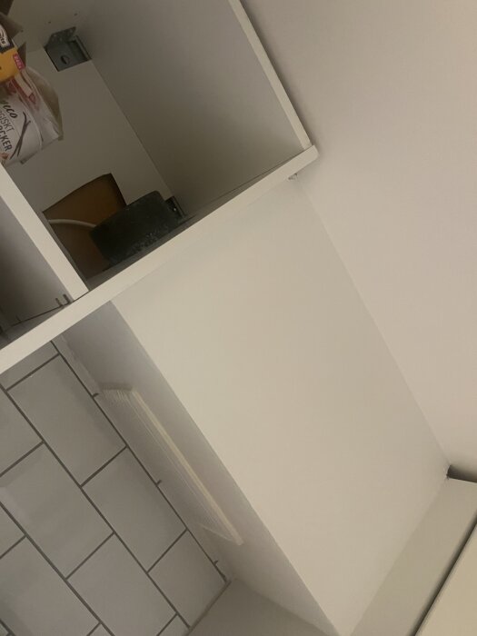 OVK-besiktning: Ventilationsdon bakom vit panel och kakel i kök, svår att justera och rengöra; synligt utrymme ovanför panelen.