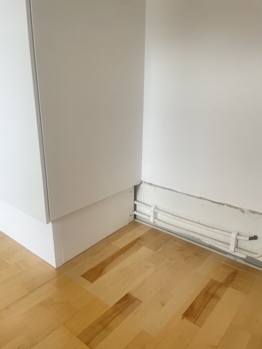 Garderob placerad i en lägenhet med synliga rör längs väggen och träparkettgolv.