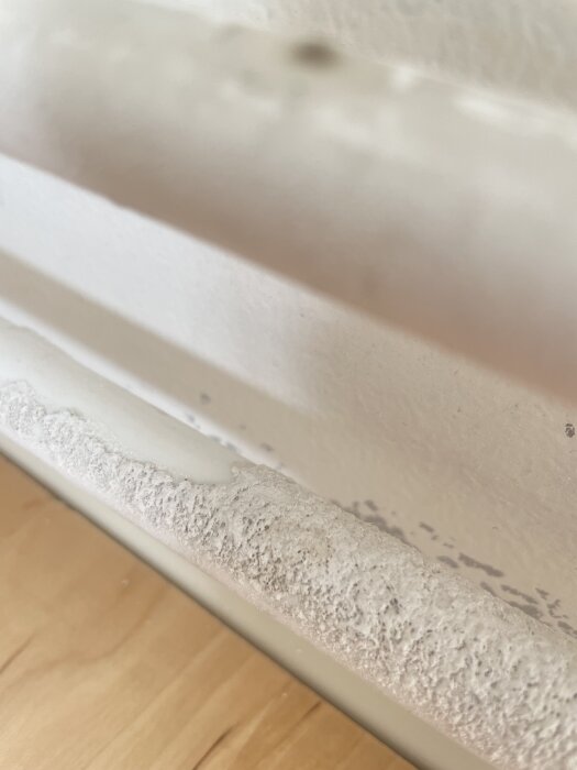 Vitt vattenrör med oregelbunden yta, osäkert om det är mögel eller torkad färg; rör ovanpå ljust trägolv.