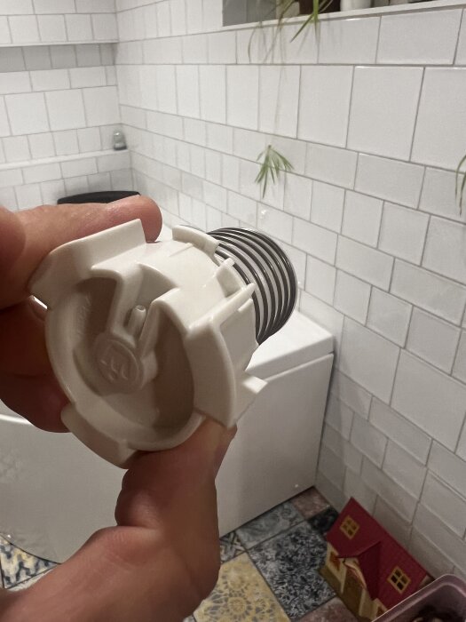 Närbild på en hand som håller en vit spolknappsats i ett kaklat badrum.