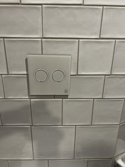 Vitt kakel med en monterad spolknappsats med två knappar, nu komplett och fungerande efter att ha fått en reservdel.