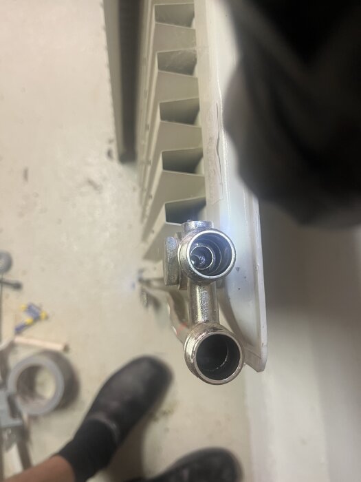 Två röranslutningar på radiator, vänstra röret skiljer sig från det högra, vy ovanifrån med del av radiator synlig i bakgrunden.