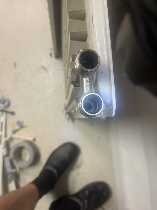 Två röranslutningar på en radiator, den vänstra har en annorlunda design jämfört med den högra.